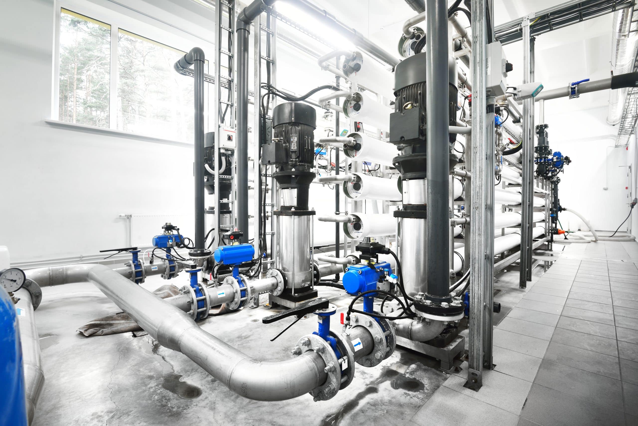 Large industrial water treatment and boiler room. Shiny steel metal pipes and blue pupms and valves.